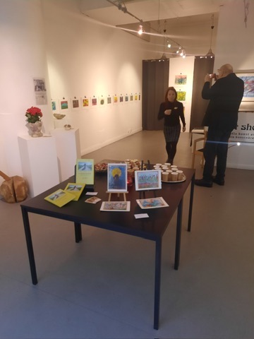 Gallerirum med små akvareller av Kaj Utter längs väggarna och ett bord med böcker och kort
