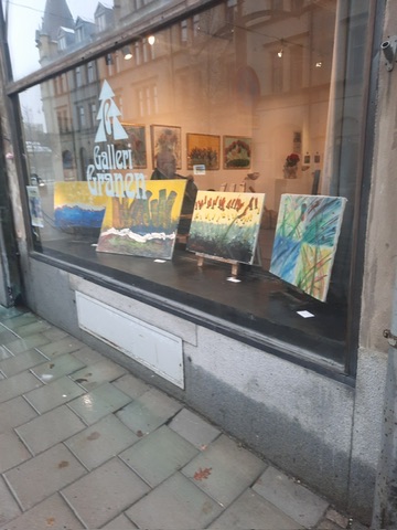 Skyltfönstret på Galleri Granen med akvareller av Kaj Utter på stafflier och galleriets logotyp i glaset